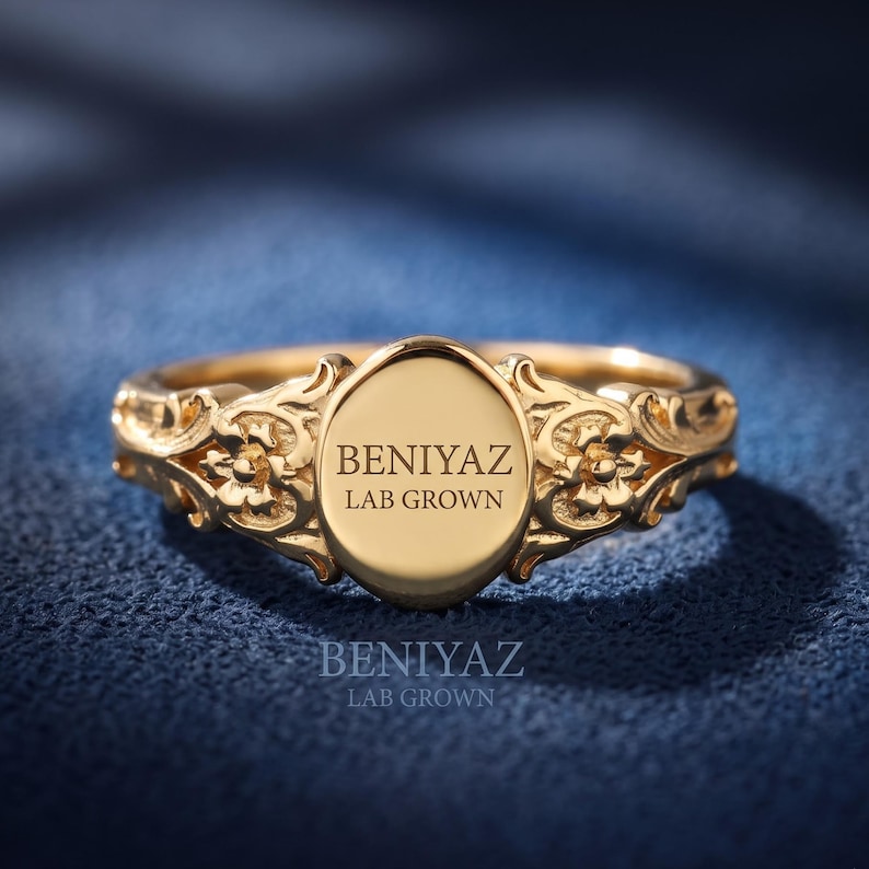 Personalized vintage floral oval signet ring in yellow gold with an ornate engraved face and decorative scrollwork shoulders.