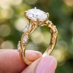 Side profile of oval engagement ring showing the raised lab grown diamond center, accent stones and dainty polished gold band.