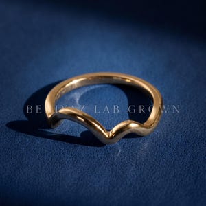 Hand held rear view of a curved V contour wedding band showing the plain polished gold shank and nesting shape.