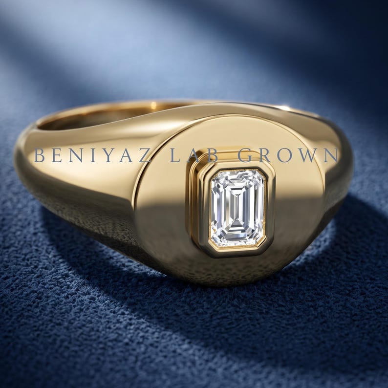 Yellow gold emerald cut lab grown diamond signet ring on blue fabric, showing the rounded face and tapered shoulders.