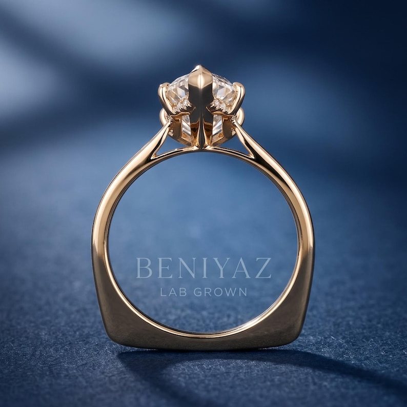 Op de afbeelding: Een gouden ring met een enkele, gefacetteerde, heldere, rondgeslepen steen in een zeskantige zetting. De ringband is glad en gepolijst. De tekst BENIYAZ LAB GROWN staat in het wit gedrukt in het midden van de ringband op de donkerblauwe achtergrond.