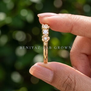 May include: A gold ring featuring two small, round, clear stones set within flower-shaped metal settings. The band is smooth and polished gold. The text BENIYAZ LAB GROWN is printed across the center of the image in white capital letters.