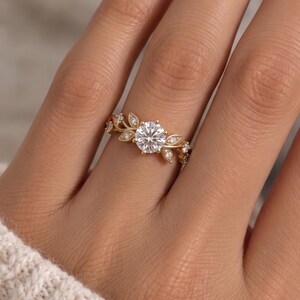 Nature inspired lab grown diamond ring worn on hand, featuring a round brilliant center and delicate botanical leaf shoulders.
