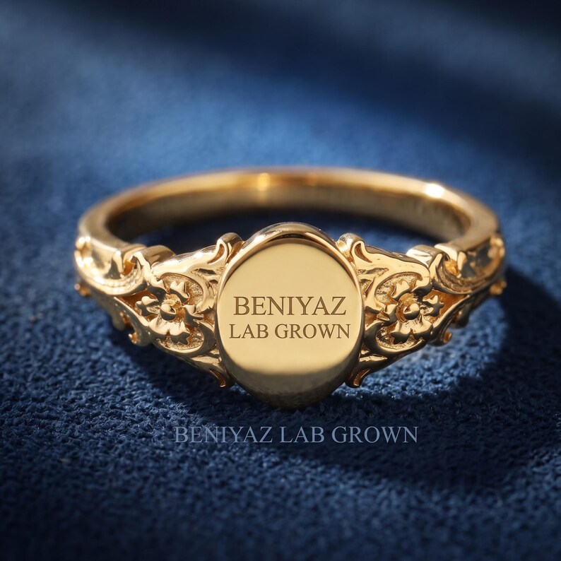 Engraved oval signet ring in yellow gold with personalized front text and ornate floral shoulder detailing.