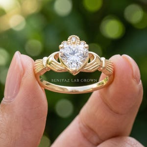 Front studio view of a yellow gold Claddagh ring with heart cut lab grown diamond center and detailed crown and hands motif.