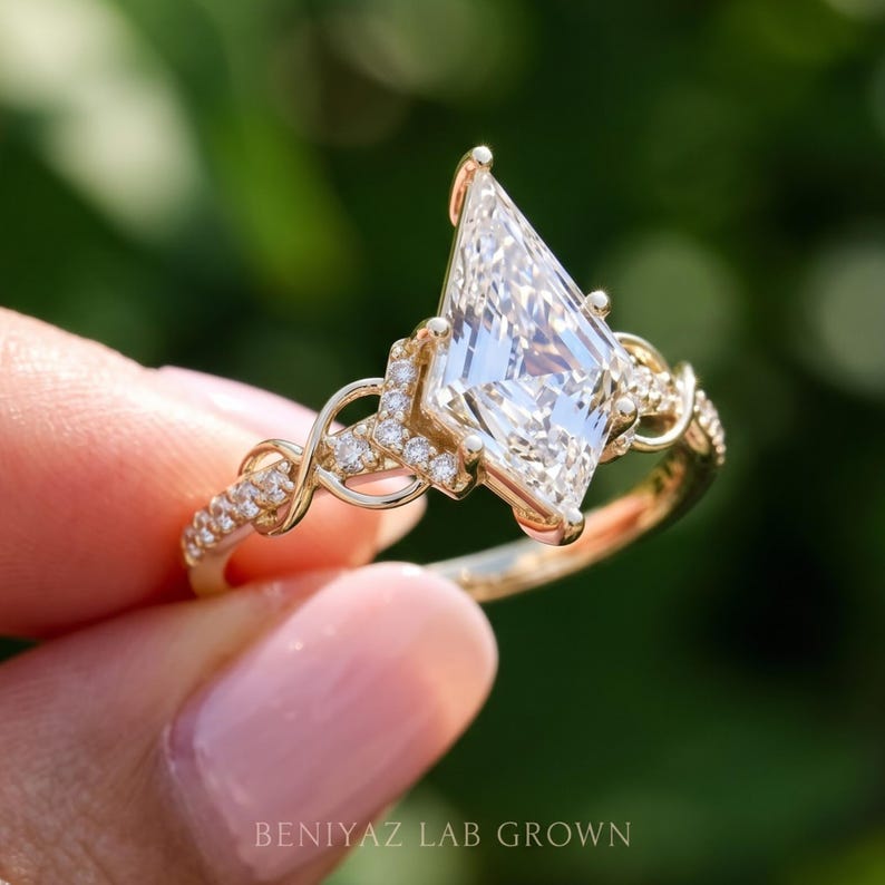 Three-quarter profile photograph of a kite cut diamond ring held between fingertips. This view highlights the elevated geometric center stone, intricate side setting and twisting pavé diamond accents along the warm gold tone engagement ring band.