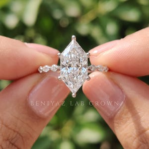 Front view of a Dutch marquise lab grown diamond ring held between fingers, featuring a sparkling elongated solitaire diamond with marquise and round diamond accents along the slim band.