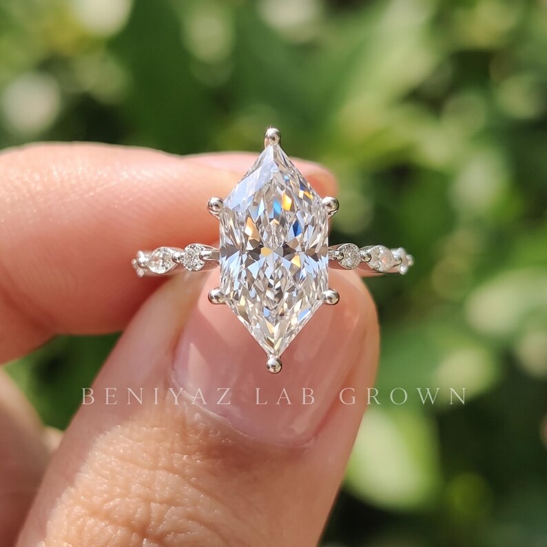 Macro photograph of a Dutch marquise cut lab grown diamond engagement ring held between fingertips, displaying the pointed elongated diamond, precise six prong setting and brilliant facets.