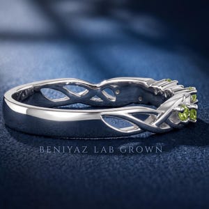 Side view of a nature inspired peridot band showing open vine work, leaf details and green round stones.