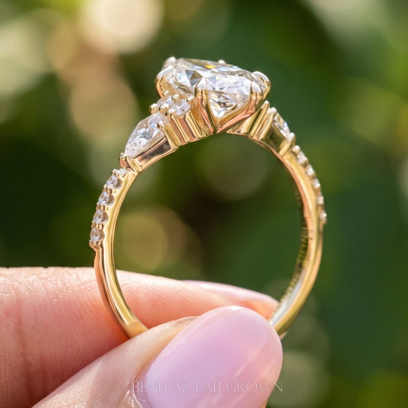 Full circular profile of a marquise engagement ring held between fingertips outdoors. The photograph shows the raised diamond cluster, decorative gallery, accent stones along the shoulders and polished gold tone band.