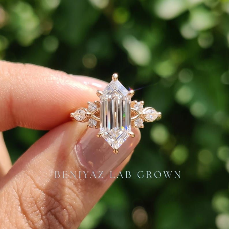 Elongated hexagon diamond ring held between fingers showing geometric seven stone setting and polished yellow gold shank