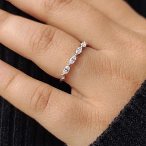 Close-up lifestyle photograph of a woman wearing a delicate marquise and round lab grown diamond ring. The elegant slim band sparkles on her finger, styled with a black sleeve for a minimalist everyday jewelry look.