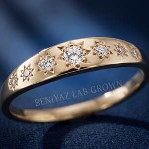 Close up celestial diamond band on blue background showing seven starburst set lab grown diamonds in graduated sizes