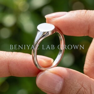 Close up petite oval signet ring held between fingers with blank polished oval face and slim tapered shoulders