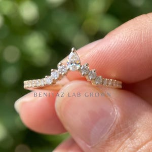 Close up hand view of a 14K yellow gold curved wedding band with pear and round lab grown diamonds in a chevron contour nesting design