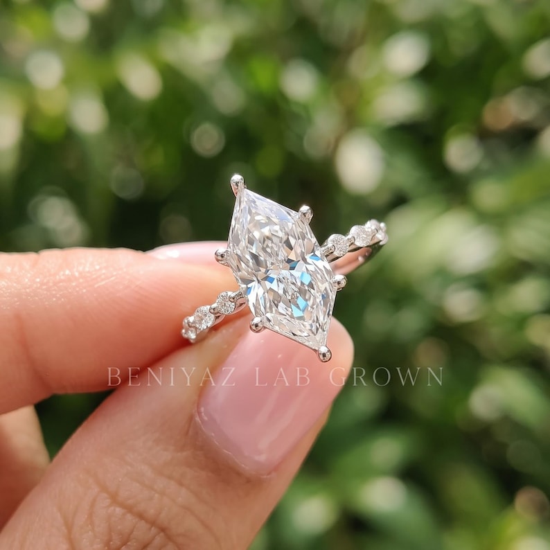 Dutch marquise engagement ring with lab grown diamond in six prong setting and marquise and round diamond band, held between fingers