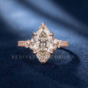 Close up of a marquise lab grown diamond engagement ring held outdoors, showing the large centre diamond and round side accents.