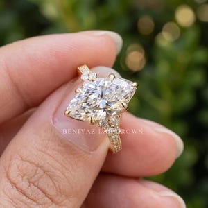 Hand held front angle of a 3 CT marquise diamond engagement ring showing the elongated centre and sparkling side diamonds.