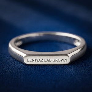 Personalized flat top ring held between fingers, showing the slim side profile and smooth engraving surface.