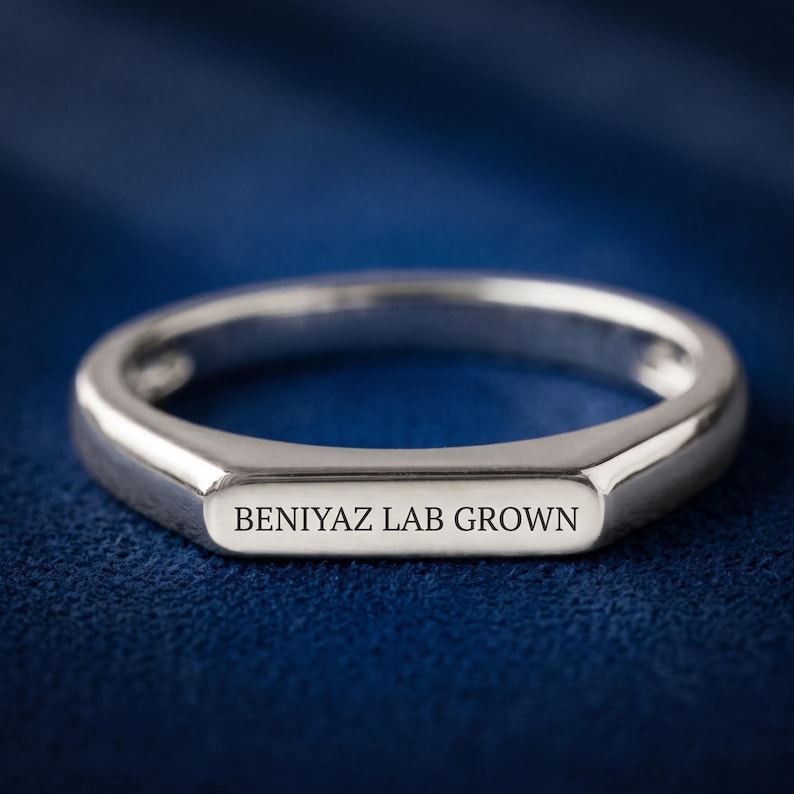 Personalized flat top ring held between fingers, showing the slim side profile and smooth engraving surface.