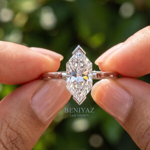 Front close up of Dutch marquise ring with sparkling lab grown diamond solitaire held between fingers against a green background.