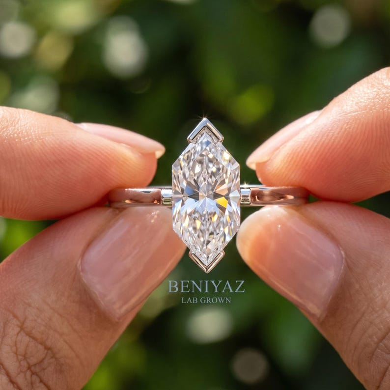Front close up of Dutch marquise ring with sparkling lab grown diamond solitaire held between fingers against a green background.