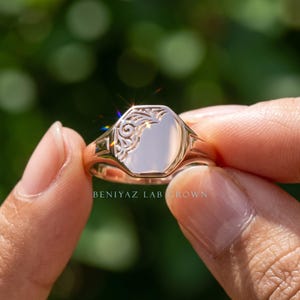 Yellow gold personalized oval signet ring held by hand with smooth engraving face and vintage floral scrollwork design