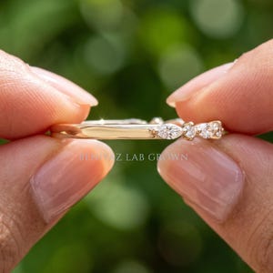 Close up side angle of lab grown diamond wedding band held between fingers with alternating marquise and round stones