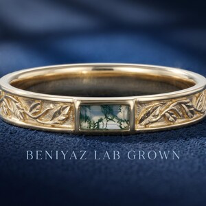Puede incluir: Un anillo de oro con una piedra de &aacute;gata musgosa rectangular con inclusiones verdes, engastada entre bandas grabadas con un patr&oacute;n de hojas. El texto BENIYAZ LAB GROWN es visible debajo del anillo, que tiene un acabado pulido.