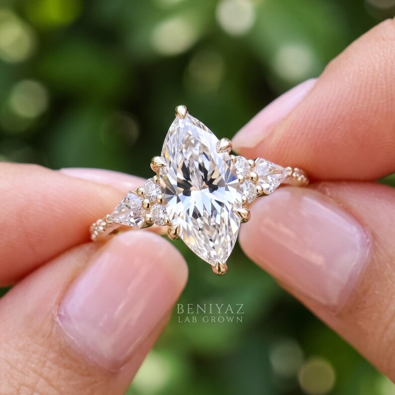 Front view of a marquise lab grown diamond engagement ring held gently between fingertips. The sparkling center stone and symmetrical cluster of smaller accent diamonds create an intricate vintage inspired bridal design.