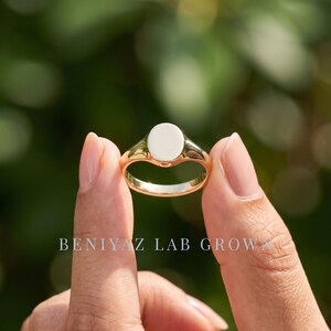 Small oval signet ring held by hand with smooth blank face, delicate tapered shank and clean minimalist styling