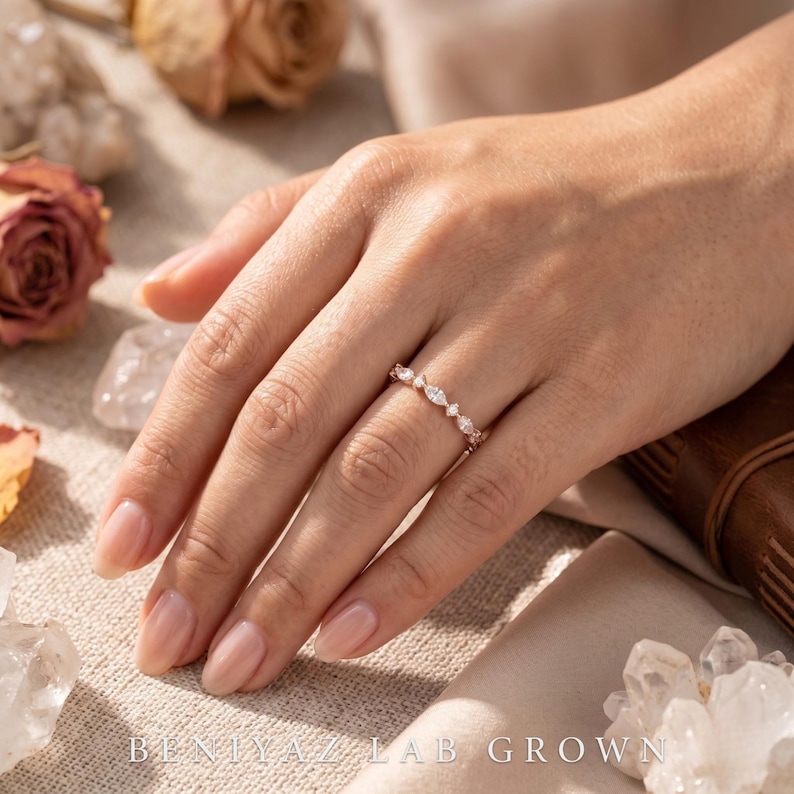 Woman wearing a dainty marquise and round lab grown diamond wedding band on finger in a bridal lifestyle setting