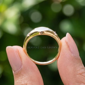 Hand holding a custom engraved gold ring showing the full band profile, personalized detail and clean polished finish against soft green foliage