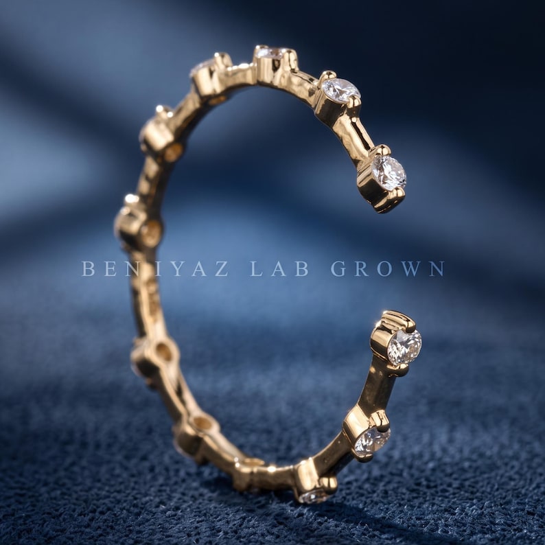 May include: A gold open-style ring featuring a series of round, clear, lab-grown stones set along the band. The text BEN IYAZ LAB GROWN is visible in the center of the ring. The band has a polished finish and a circular, incomplete design.