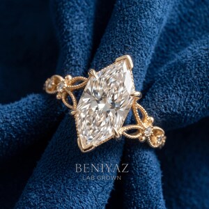 May include: A gold ring featuring a large marquise-cut center stone and smaller accent stones along the band. The band has an intricate, openwork metal design. The text BENIYAZ LAB GROWN is printed in white at the bottom of the image.
