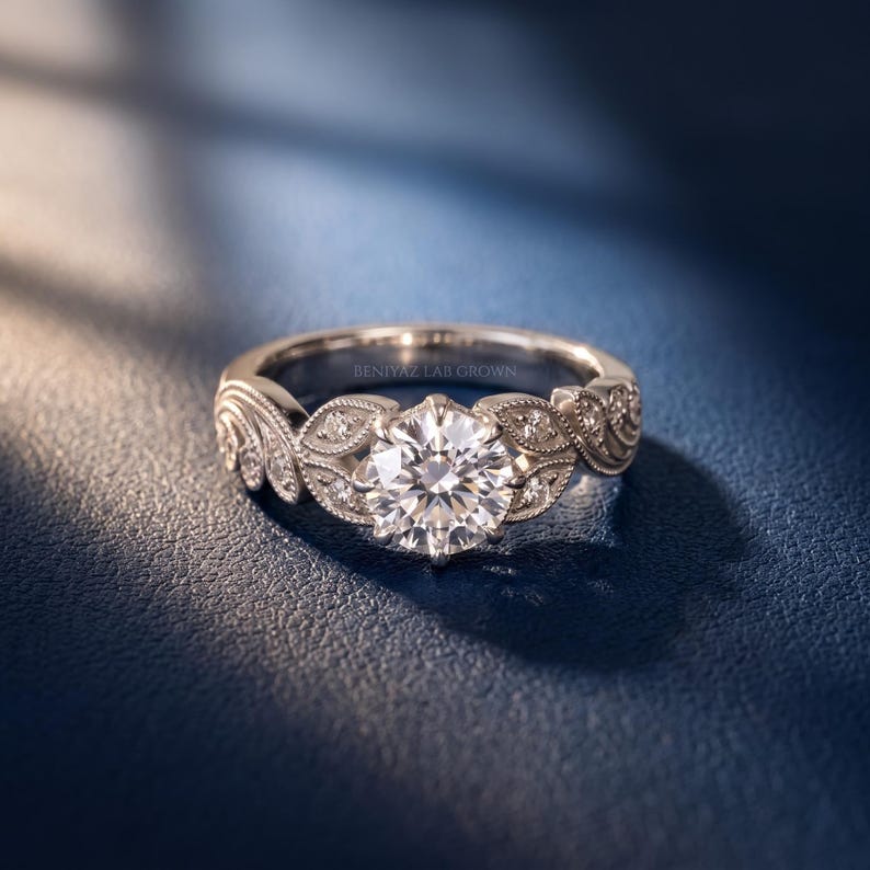 White gold round lab grown diamond engagement ring with a large brilliant center stone, vintage floral leaf detailing, milgrain accents and side diamonds, shown from an angled side view.