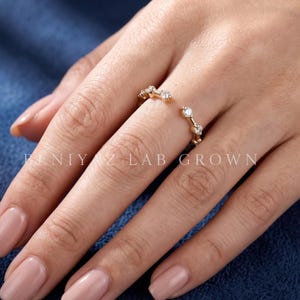 May include: An open-style gold ring featuring a series of small, clear, round-cut stones set along the band. The text BENIY Z LAB GROWN is visible across the center of the image. The ring is worn on a finger, showcasing the delicate metal design.