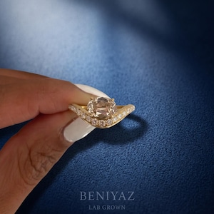 Close-up natural hand photo showing an oval lab grown diamond engagement ring in yellow gold with a curved crossover pavé band and elegant bridal style.