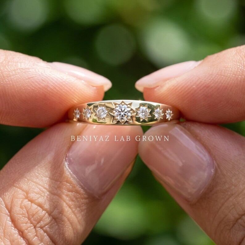 Star set lab grown diamond ring held between fingers with seven celestial star motifs and smooth polished gold band