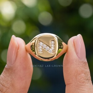 Personalized lab grown diamond initial ring held between fingers, yellow gold signet jewelry with modern geometric letter design