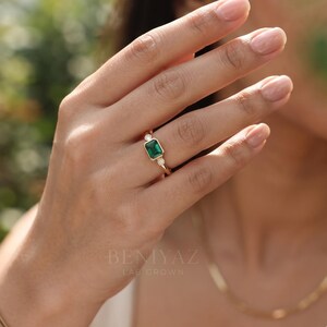 Lab grown emerald engagement ring worn on hand, featuring an east west emerald cut center and lab grown diamond side stones.
