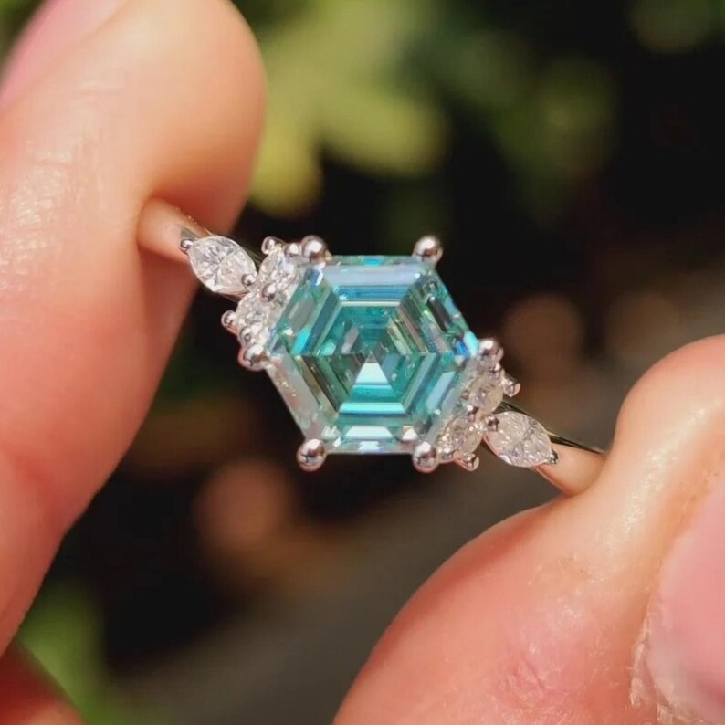 Detailed angle of hexagon step cut moissanite engagement ring with VVS cyan blue center stone and colorless side accents.