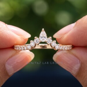 Hand displaying a lab grown diamond contour band in yellow gold with pear and round diamond accents, curved chevron wedding ring for stacking