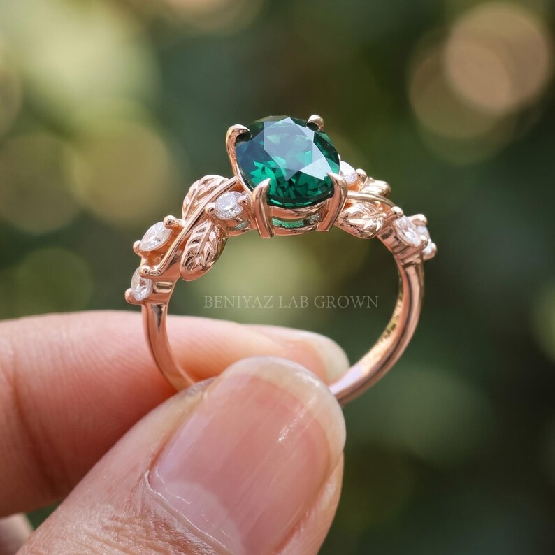 Close angled view of oval emerald ring with green center gemstone, leaf motifs and sparkling accent stones.