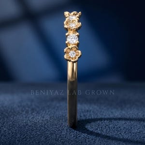 May include: A gold ring featuring a series of four flower-shaped settings, each containing a small round brilliant-cut diamond. The band is smooth and polished. The text BENIYAZ LAB GROWN is visible in the center of the image.