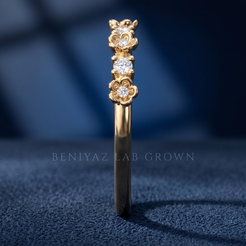 May include: A gold ring featuring a series of four flower-shaped settings, each containing a small round brilliant-cut diamond. The band is smooth and polished. The text BENIYAZ LAB GROWN is visible in the center of the image.