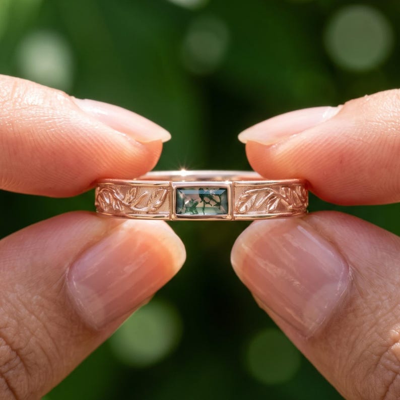 Puede incluir: Un anillo de oro rosa con una piedra preciosa de &aacute;gata musgosa rectangular de corte baguette en el centro. La banda presenta un patr&oacute;n en relieve detallado de hojas y enredaderas que se extienden desde el engaste central a lo largo del aro.