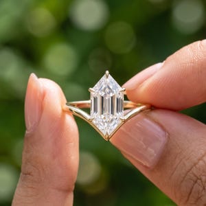 Close up hand held view of a Dutch Marquise lab grown diamond solitaire ring with an elongated center stone and gold band.