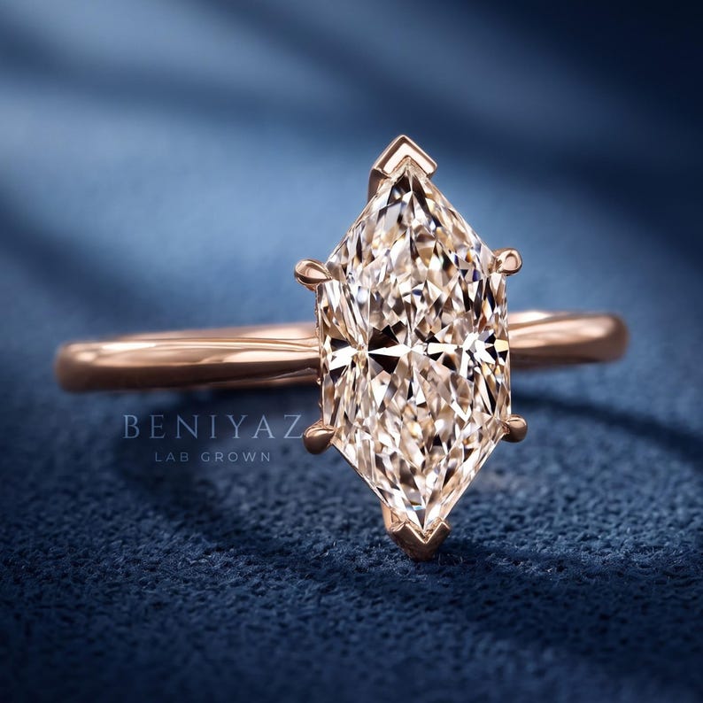 Op de afbeelding: Een ros&eacute;gouden ring met een centraal geplaatste marquise-geslepen steen, vastgezet met zes pootjes. De ringband is glad en gepolijst. De tekst BENIYAZ LAB GROWN is zichtbaar aan de linkerzijde van de ring. Het ontwerp benadrukt de langwerpige vorm.