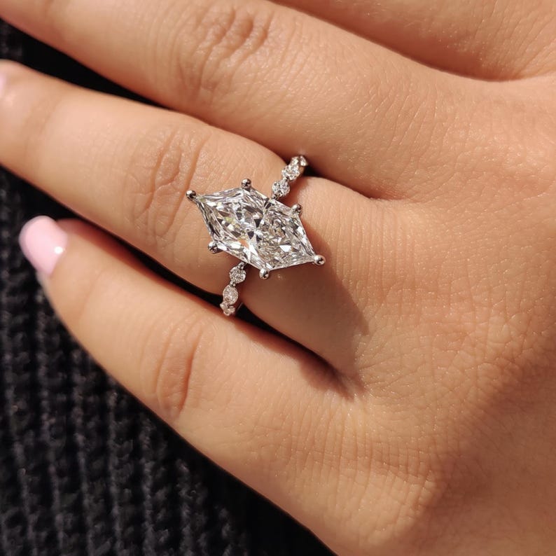Woman wearing an elongated Dutch marquise lab grown diamond engagement ring with a six prong solitaire setting and small diamond accents, photographed in a natural close-up hand pose.